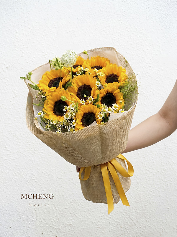Bó Hoa Tốt Nghiệp Hướng Dương Phối Cúc Họa Mi Tươi Trẻ - Mcheng Florist Góc nghiêng tôn lên lớp giấy lưới thô mộc mạc và nơ vàng của bó hoa tốt nghiệp